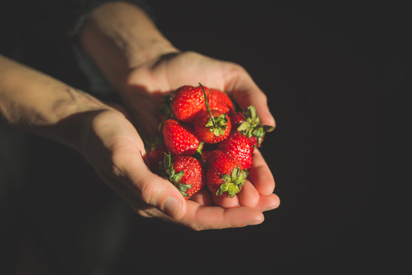 Hands offering strawberries.